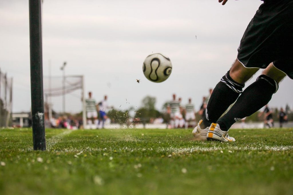 Trainer helpt speler bij voetbalvaardigheden stimuleren door basistechnieken dribbelen en passen te oefenen op voetbalveld